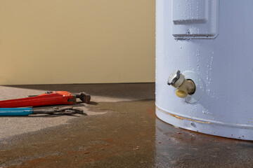 Water leaking from a residential electric water heater with a couple plumbers tools. - obrazy, fototapety, plakaty