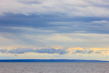 Naklejka na ściany i meble Early morning clouds over distant land, viewed offshore in calm ocean