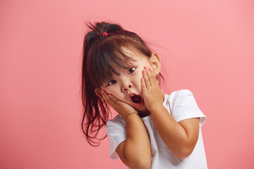 Headshot of stupefied little girl keeps hands on cheeks standing over pink isolated background....