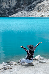 Girl wearing a black hat and black and white striped sweater next to a turquoise high mountain lagoon