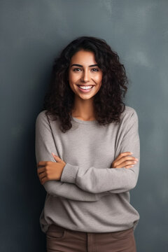 Portrait of a young latin woman with pleasant smile and crossed arms isolated on grey wall.