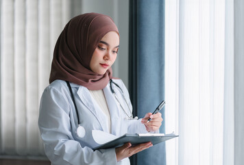 smiling muslim female doctor in brown hijab carrying medical records. - obrazy, fototapety, plakaty