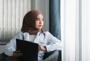 smiling muslim female doctor in brown hijab carrying medical records.