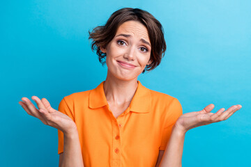 Photo of doubtful unsure girl dressed orange polo shrugging shoulders isolated blue color background