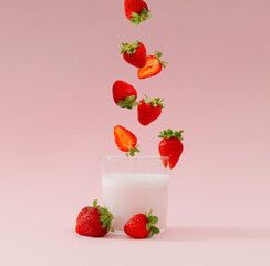 Creative layout made of strawberries falling into glass cup of milk drink with strawberry taste on...