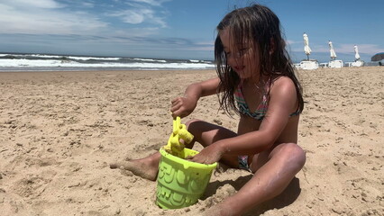 Little girl child playing with sand and bucket at beach shore