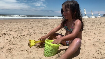 Little girl child playing with sand and bucket at beach shore