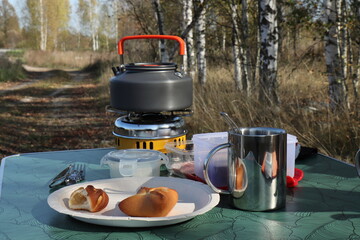 A metal mug with pies and a gas burner on a folding tourist table against the backdrop of a field...