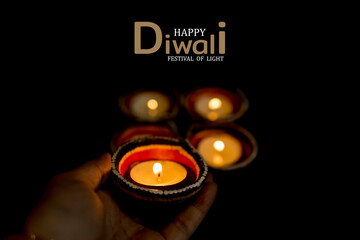 Happy Diwali - Woman hands with henna holding lit candle isolated on dark background.