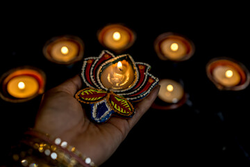 Happy Diwali - Woman hands with henna holding lit candle isolated on dark background.