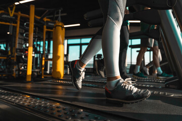 Unrecognizable athletes running on treadmills in health club. Bellow knees view of female legs captured in motion while doing cardio.