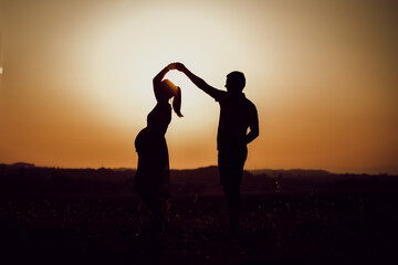 Photographie d'une silhouette d'un homme et d'une femme enceinte entrain de danser au coucher de...