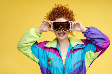Portrait of beautiful smiling curly woman wearing ski overalls, hat, protective ski mask