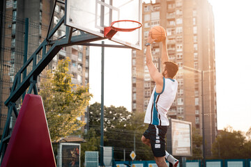 Young male basketball player dunking in outdoors court. Sports athlete performing slam dunk on the...