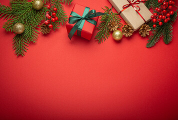 Christmas or New Year celebration red paper festive background with decoration fir tree, wrapped present boxes, cones, berries, sparkly red balls. Space for text..