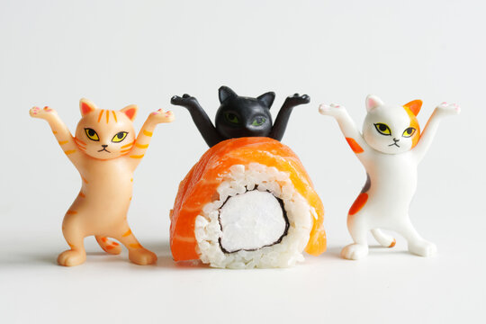 Piece of Philadelphia roll next to funny toy dancing kittens with raised paws. Photo. Macro. Selective focus. Daylight