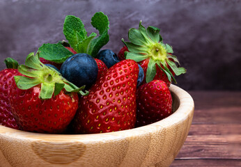 Delicious red strawberries and blueberries in a wooden bowl placed on a table. Selective focus.