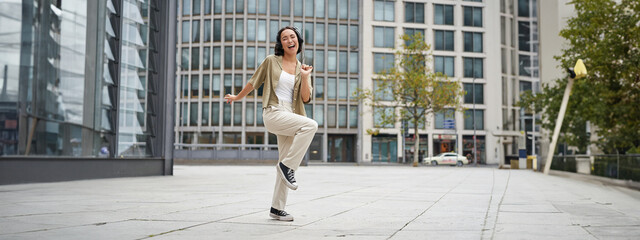 Happy people in city. Upbeat young girl dancing on street in headphones, listening music in headphones