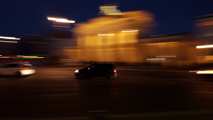 A sleek car glides through the dimly lit street, its headlights creating illuminating streaks of...