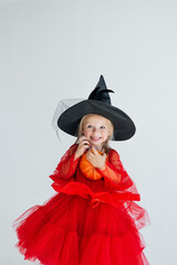 A little witch in a pointed hat holds a pumpkin. A child in a festive carnival Halloween costume...