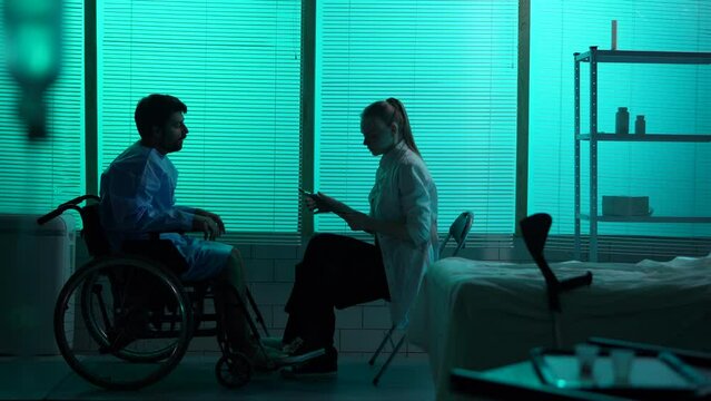 Full-sized silhouette video a disabled man, patient with mobility impairment on a wheelchair talking to a female doctor who tells him bad news. The man is shocked and desperate.