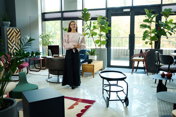 Beautiful young woman stands in a spacious, bright room
