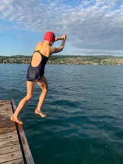 Mädchen in Badekleid und mit Bademütze springt in den See