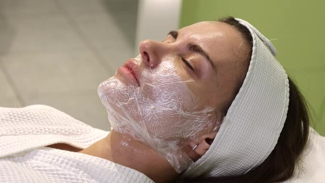Cosmetologist applying cream with anesthesia on patient's face, portrait closeup view. Preparing skin for biorevitalization or thread lifting procedure. Woman in beauty clinic with doctor beautician.