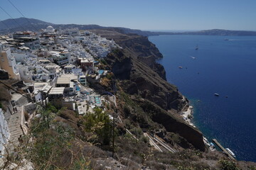 Fototapeta na wymiar A view of the blue and white terraced houses of Santorini from the town of Fira at the top of the mountain. To the right is the azure blue sea and the mountain massif forming the island. 