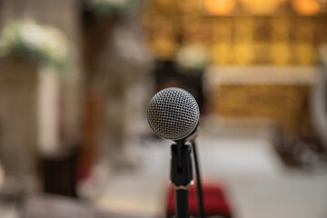 Microphone in the foreground ready to be used inside a church or religious space. Blurred church background.