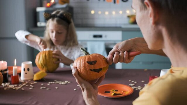 Close-up of father with little daughter carving Halloween pumpkins in the kitchen, slow motion. Selective focus. Preparing and decorating for holidays