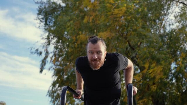 Caucasian man doing parallel bars exercises outdoors in autumn. Slow motion. 