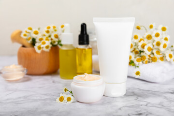 Chamomile spa. Composition with chamomile flowers, handmade soap, essential oil cosmetic bottle, body cream, scrub and sea salt on a white texture background. Relaxing beauty treatments.Copy space