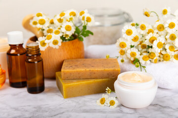 Chamomile spa. Composition with chamomile flowers, handmade soap, essential oil cosmetic bottle, body cream, scrub and sea salt on a white texture background. Relaxing beauty treatments.Copy space