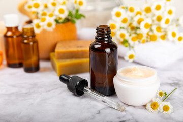 Chamomile spa. Composition with chamomile flowers, handmade soap, essential oil cosmetic bottle, body cream, scrub and sea salt on a white texture background. Relaxing beauty treatments.Copy space