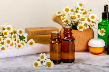 Chamomile spa. Composition with chamomile flowers, handmade soap, essential oil cosmetic bottle, body cream, scrub and sea salt on a white texture background. Relaxing beauty treatments.Copy space