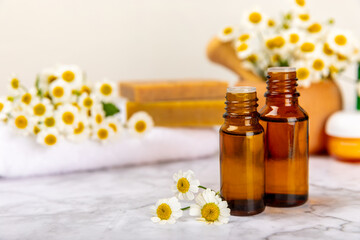 Chamomile spa. Composition with chamomile flowers, handmade soap, essential oil cosmetic bottle, body cream, scrub and sea salt on a white texture background. Relaxing beauty treatments.Copy space