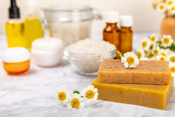 Chamomile spa. Composition with chamomile flowers, handmade soap, essential oil cosmetic bottle, body cream, scrub and sea salt on a white texture background. Relaxing beauty treatments.Copy space