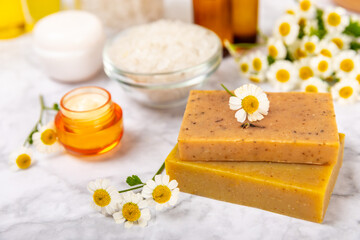 Chamomile spa. Composition with chamomile flowers, handmade soap, essential oil cosmetic bottle, body cream, scrub and sea salt on a white texture background. Relaxing beauty treatments.Copy space