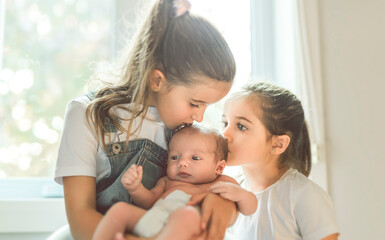 two sisters sit on bedroom with newborn son at home