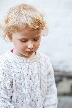 Little sad girl girl in white sweater outdoors Portrait of a little curly blonde girl