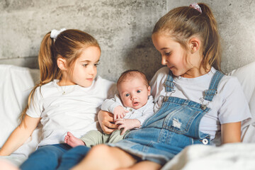 two sisters sit on bedroom with newborn son at home