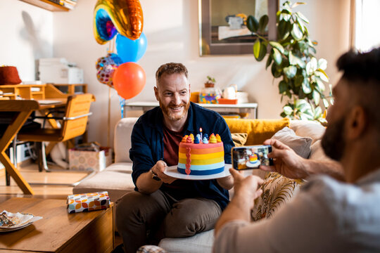 Young man celebrating his birthday and getting a picture taken from his gay partner in the living room at home