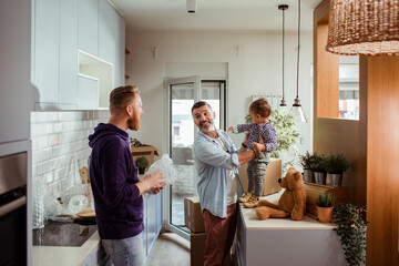 Young male gay couple playing with their son in the kitchen of their new apartment