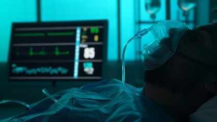 Close-up detail shot of a patient on breathing support dying in a hospital bed. His ICU monitor on...