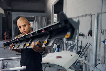 Car factory worker carrying iron beam that will serve as fender or threshold