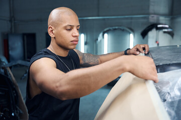 Focused automobile mechanic covering car parts with special protective paper