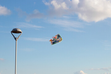 Sun illuminating a lone colorful rainbow kite flying high against puffy white clouds in a blue sky