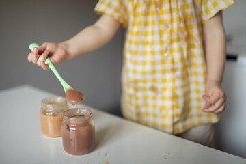 The child holds in his hand a spoon with fruit puree from a jar.