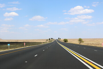 Obraz premium The N3 freeway from Johannesburg to Durban in South Africa, straight road to the horizon over dry landscape with cars and trucks from drivers point of view
